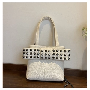 Close-up of white lychee leather bag featuring a studded bow and metal chain strap