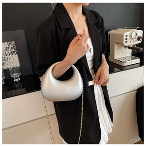 Detail of silver crescent acrylic clutch with golden chain strap on a model shoulder