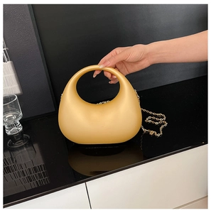 Détail d'un sac à main en acrylique jaune mat avec poignée ronde et bandoulière en chaîne dorée