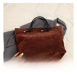 Detail of burgundy suede tote bag featuring black knotted cord and round top handle