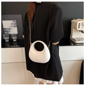 Sac demi-lune blanc minimaliste en cuir porté par un modèle avec chaîne dorée