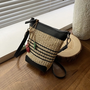 Detail of woven straw bucket bag with black leather trim and cute red cherry charm decoration