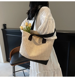 Detail of a large woven tote bag with beige straw texture and black leather handles