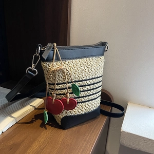 Detail of woven straw bucket bag with black stripes and a red cherry charm decoration