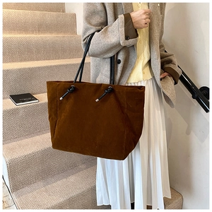 Detail of dark brown tote bag with black rope knot handle in warm studio setting