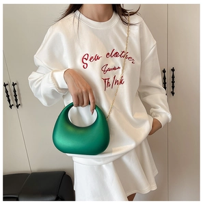 Détail du sac de soirée en acrylique vert avec chaîne dorée tenu par un mannequin en sweat