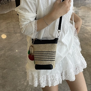 Top view of a woven straw bucket bag with black leather trim and red cherry charm detail
