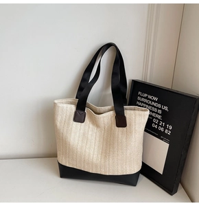 Detail of a beige woven tote bag with black leather base and wide fabric shoulder straps