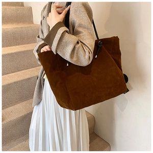 Detail of a large brown suede tote bag with black knotted handles shown in an autumn outfit