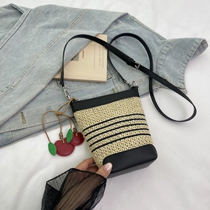 Top-down view of a woven straw bucket bag with black leather trim and cherry charm detail