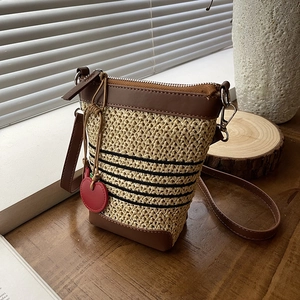 Close-up of woven straw bucket bag with red heart charm on vintage wooden table
