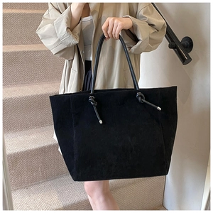 Detail of minimalist black suede tote bag featuring knot handle accents and spacious design