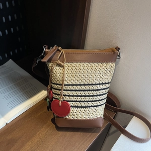 Close-up of woven straw bucket bag with black stripes and red cherry charm on desk