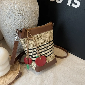 Detail of straw woven bucket bag with black stripes and red cherry pendants