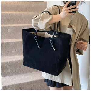 Detail of matte black suede tote bag featuring thin leather straps and silver metal tips