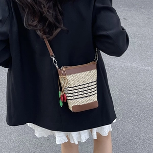 Detail of woven crossbody bucket bag with brown leather trim and cherry charm