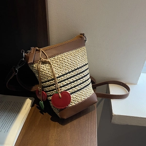 Detail of woven straw bucket bag featuring red cherry charms and brown leather trim