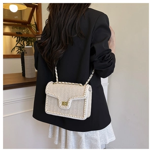 Gros plan d'un sac bandoulière beige tissé avec bordure en perles et fermoir doré