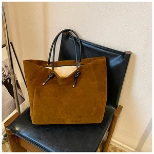 Detail of caramel suede tote bag with black leather handles on a minimalist chair