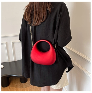 Detail of red crescent acrylic clutch with gold chain strap shown on black shirt
