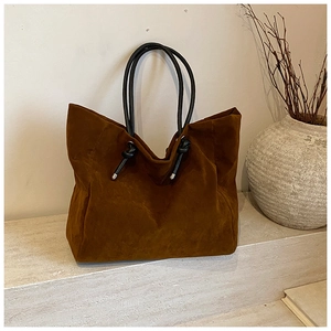 Detail of a brown suede tote bag featuring black tubular handles and knot accents