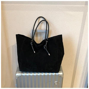 Detail of black suede tote bag with leather knot charm on a silver suitcase