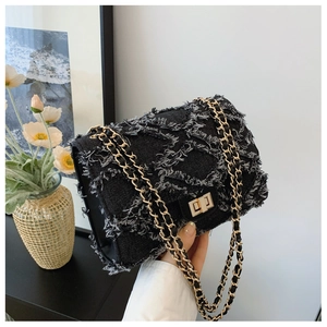 Detail of black denim quilted bag with frayed edges and golden chain strap in hands