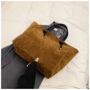 Detail of brown suede tote bag featuring black woven rope handles and silver metal accents