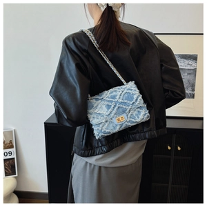 Detail of light blue denim chain bag with quilted diamond pattern on a model