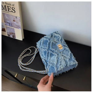 Detailed close-up of blue denim quilted bag with frayed edges and golden metal chain