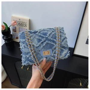 Detail of denim quilted crossbody bag with frayed edges and metallic chain strap