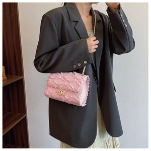 Pink denim chain crossbody bag with gold lock and tassel texture on a gray suit