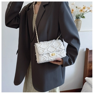 Detail of white quilted chain bag featuring frayed edges and a gold-tone swivel lock
