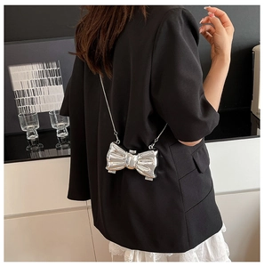 Detail view of a silver bow-shaped crossbody bag with metallic chain on model