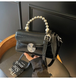Detail of glossy black leather handbag featuring a large pearl and silver bead handle