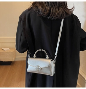 Detail of silver metallic handbag with pearl handle and round hollow metal lock buckle