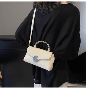 Detail of cream crossbody bag featuring pearl handle, metal buckle and crocodile texture