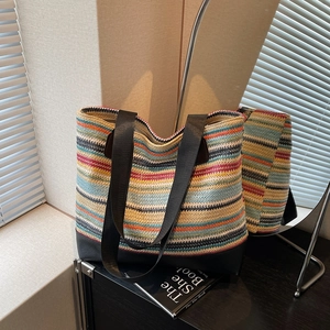 Colorful woven stripe tote bag with black handles displayed on a desk with a magazine