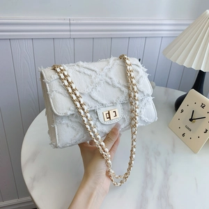 White denim crossbody bag with quilted texture and gold chain strap held by a person