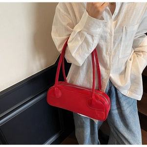 Close-up of vibrant red baguette shoulder bag worn with casual outfit and silver zipper