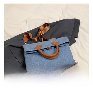 Detail of blue denim canvas bag with brown leather handles and adjustable shoulder strap