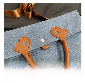 Close-up of denim tote bag with brown leather handle and gold hardware details