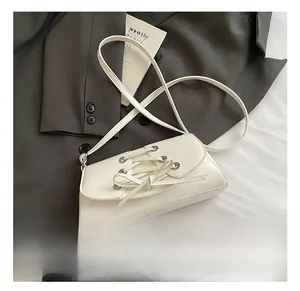 Detail of cream white faux leather shoulder bag with decorative cross strap bow on flap