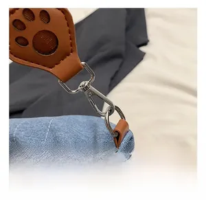 Detail of blue denim fabric with leather animal paw cutout and silver metal swivel hook