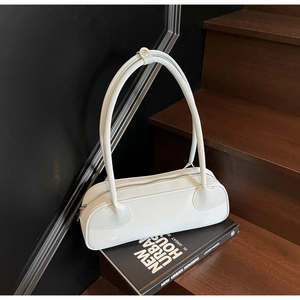 Detail of a white minimalist faux leather shoulder bag on a dark wooden staircase
