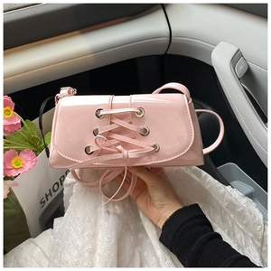 Close-up of pink patent leather shoulder bag with decorative criss-cross lacing and silver eyelets