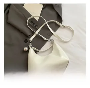 Détail du sac demi-lune en cuir verni blanc avec pendentif sphérique sur blazer gris