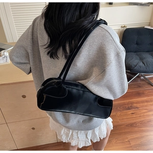 Glossy black underarm bag worn on shoulder by model in a minimalist interior setting