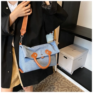 Detail of light blue denim tote bag with leather cat paw charm and wide shoulder strap