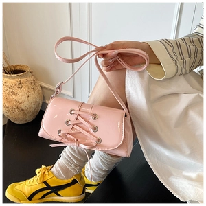 Detailed view of pink patent leather shoulder bag with lace-up ribbon design and metal eyelets
